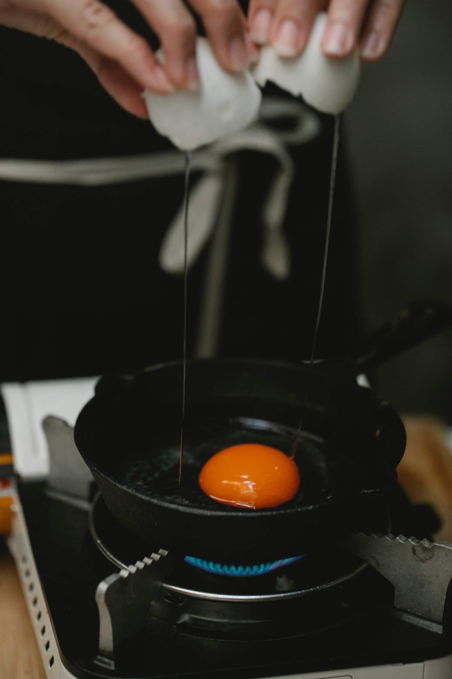 A person cooking eggs on a portable gas cooktop