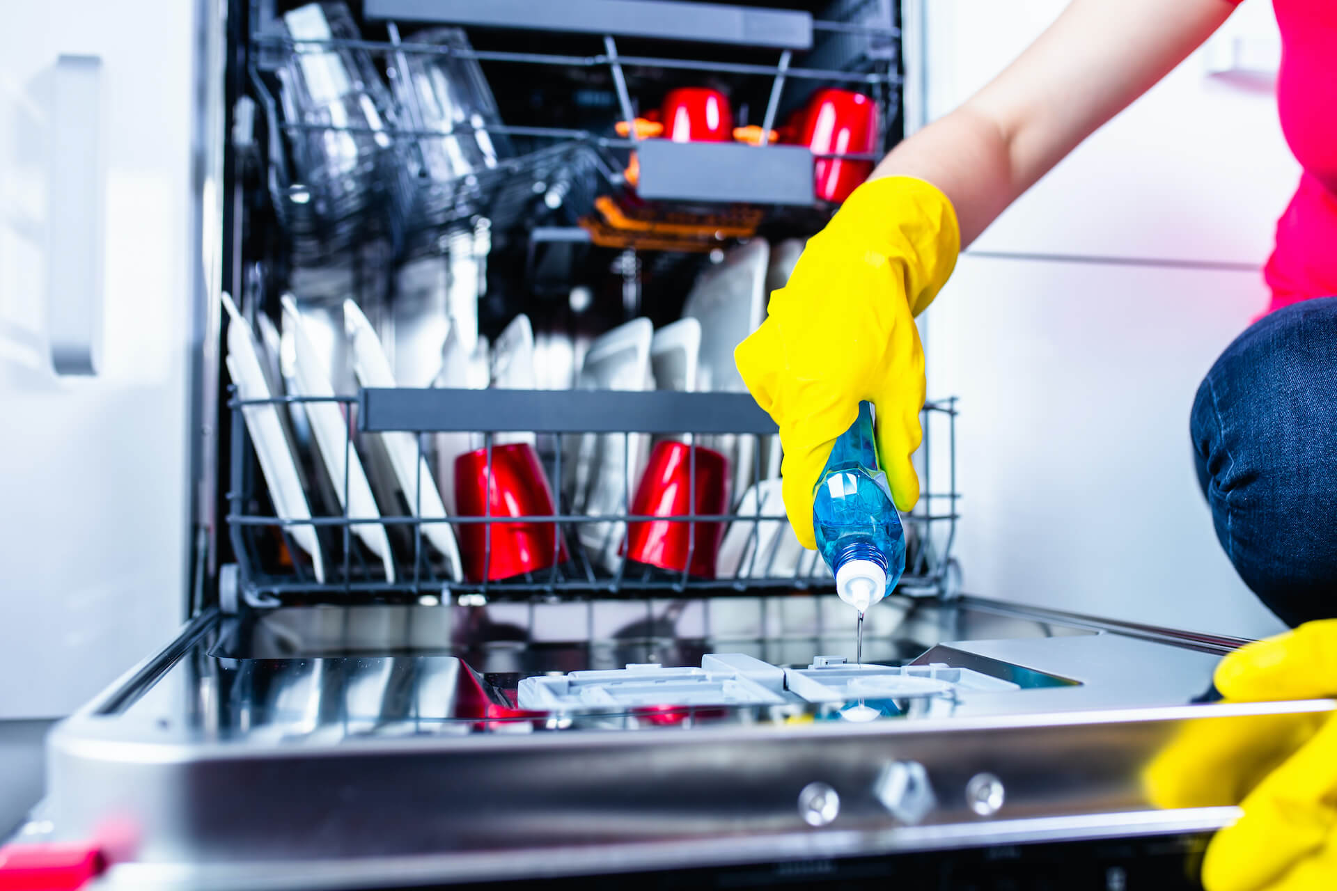 A person pouring liquid detergent inside the detergent dispenser of a loaded dishwasher