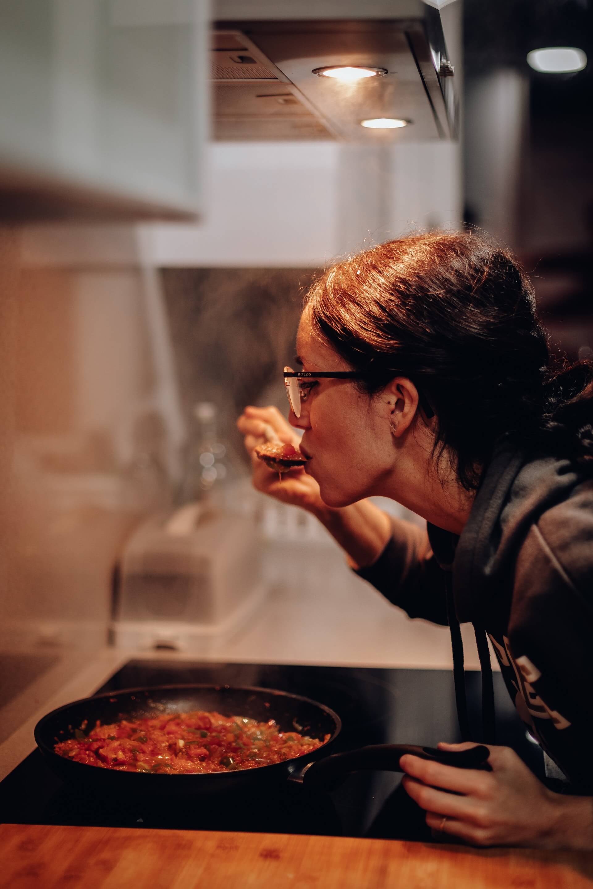 A lady tasting stir fry cooked on an induction cooktop